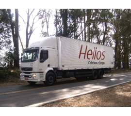 Na fotografia está um caminhão Volvo, modelo VM-270, configuração 6x2, com a cabine e o baú na cor branca, tendo a inscrição Helios em vermelho e Coletivos e Cargas em preto nas laterais e tampas traseiras. As rodas e chassi aparente estão pintados na cor preta. O prefixo deste caminhão é 604.
Imagem capturada na rodovia ERS-142 entre as cidades de Carazinho e Não me Toque no estado do Rio Grande do Sul. O cenário é árvores de pinus americano ao fundo com o céu acinzentado. 