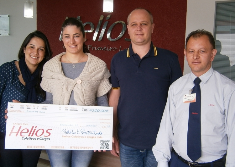 Foto com o Diretor da empresa, a associada de Palmitos/SC senhora Cristiane Manica e demais funcionários da empresa. Ao fundo a logo da empresa em fundo vermelho e letras em alumíno.