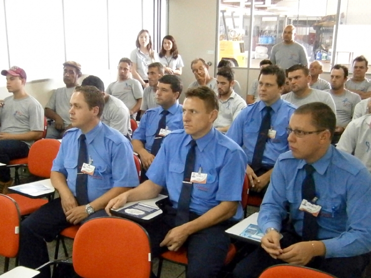 Foto dos funcionários na sede da empresa Helios atentos à palestra oferecida pelo Sest Senat. Na imagem vários motoristas com uniforme azul e pessoal de manutenção com uniforme cinza.